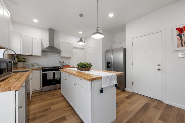 kitchen featuring stainless steel appliances, white cabinetry, wall chimney range hood, and wood counters