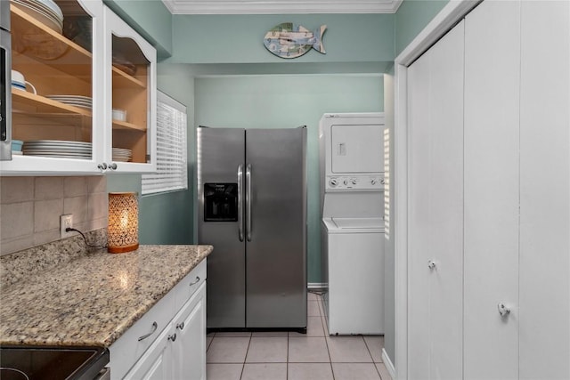 kitchen featuring stacked washing maching and dryer, tasteful backsplash, white cabinetry, light stone counters, and stainless steel fridge with ice dispenser