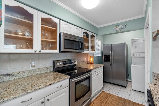 kitchen with white cabinetry, backsplash, stainless steel appliances, stacked washer / dryer, and ornamental molding