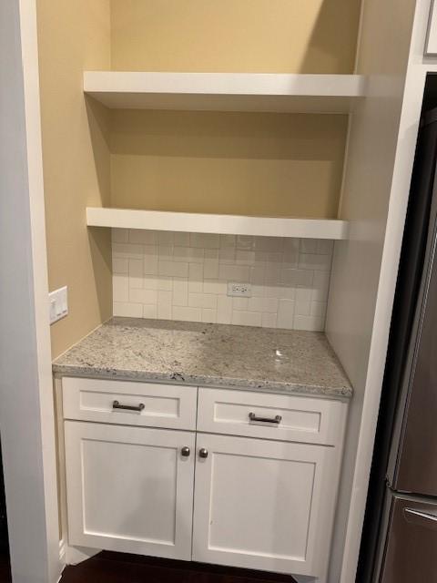 kitchen featuring light stone counters, decorative backsplash, stainless steel fridge, and white cabinets