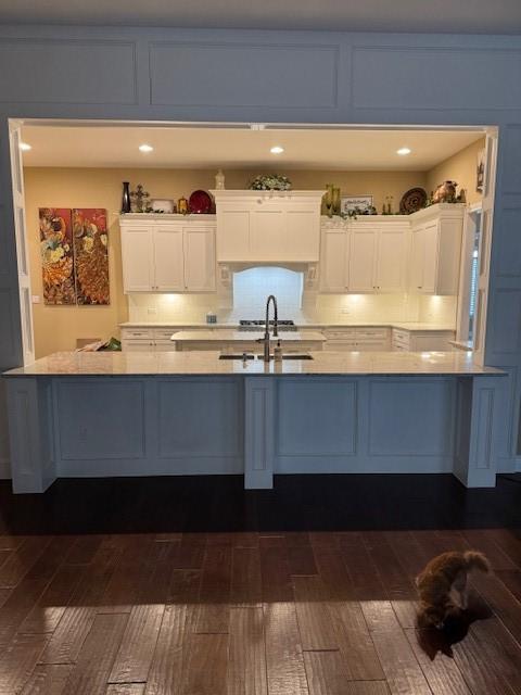 kitchen with sink, dark wood-type flooring, a breakfast bar, backsplash, and white cabinets