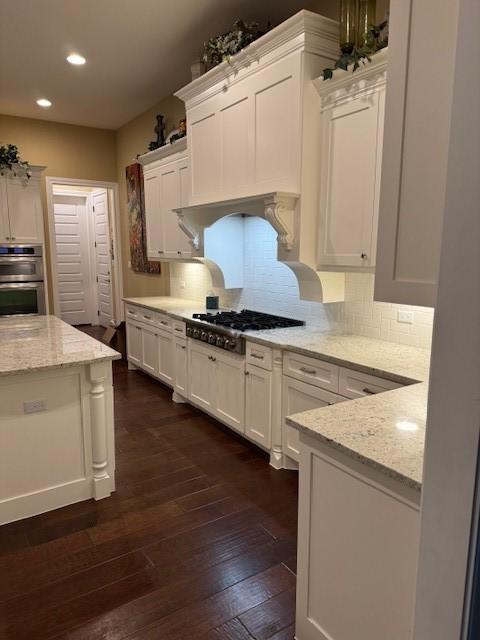 kitchen with light stone counters, tasteful backsplash, appliances with stainless steel finishes, dark hardwood / wood-style flooring, and white cabinets