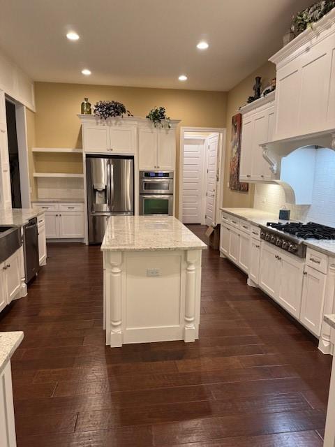 kitchen featuring white cabinetry, stainless steel appliances, dark hardwood / wood-style floors, light stone counters, and a kitchen island