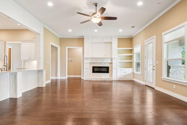124 Abamillo Dr, Bastrop, TX 78602 - unfurnished living room featuring ceiling fan, crown molding, dark wood finished floors, a stone fireplace, and recessed lighting