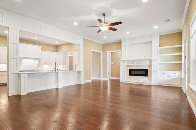 124 Abamillo Dr, Bastrop, TX 78602 - unfurnished living room with a ceiling fan, crown molding, dark wood-type flooring, a stone fireplace, and recessed lighting