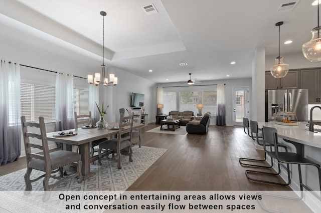 dining space with sink, a chandelier, dark hardwood / wood-style floors, and a raised ceiling