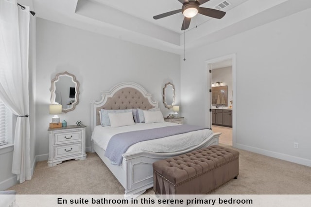 bedroom with ensuite bathroom, light carpet, ceiling fan, and a tray ceiling