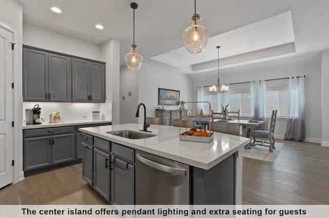 kitchen featuring decorative light fixtures, dishwasher, an island with sink, sink, and a raised ceiling