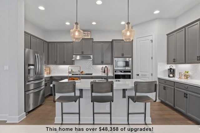 kitchen with decorative light fixtures, gray cabinets, an island with sink, and appliances with stainless steel finishes