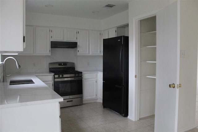 kitchen with black refrigerator, white cabinetry, sink, light tile patterned floors, and gas stove