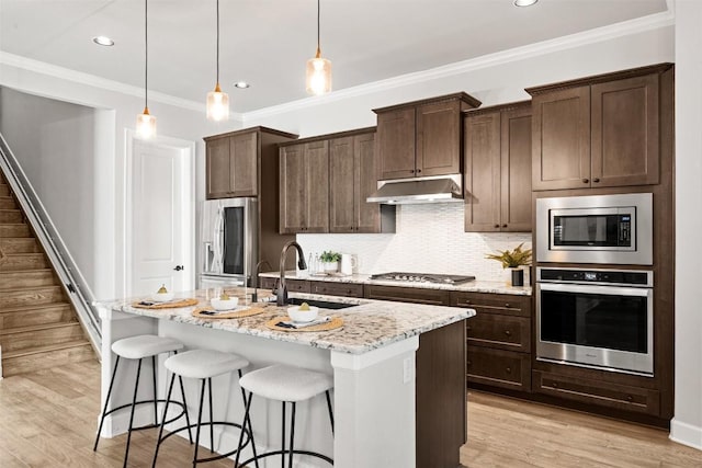 kitchen featuring a sink, under cabinet range hood, an island with sink, a kitchen bar, and appliances with stainless steel finishes