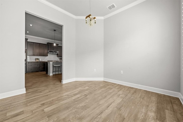 unfurnished dining area featuring baseboards, ornamental molding, light wood-style flooring, and visible vents