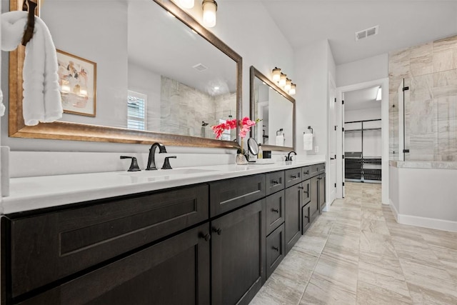 full bath featuring marble finish floor, visible vents, a sink, tiled shower, and double vanity