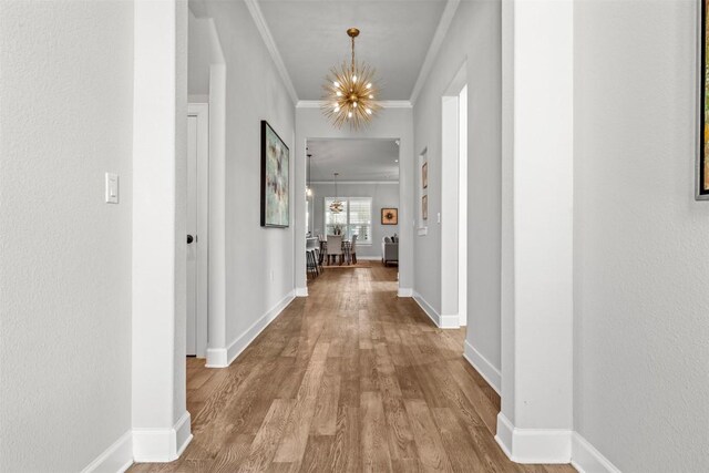 corridor with crown molding, a notable chandelier, baseboards, and wood finished floors