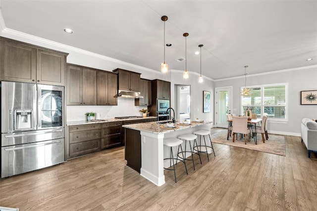 kitchen featuring dark brown cabinets, a breakfast bar, crown molding, a center island with sink, and stainless steel appliances