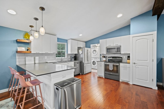 kitchen with stacked washer / drying machine, sink, white cabinetry, hanging light fixtures, and appliances with stainless steel finishes