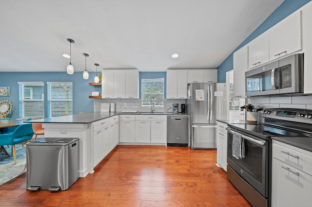 kitchen with sink, white cabinetry, stainless steel appliances, decorative backsplash, and decorative light fixtures