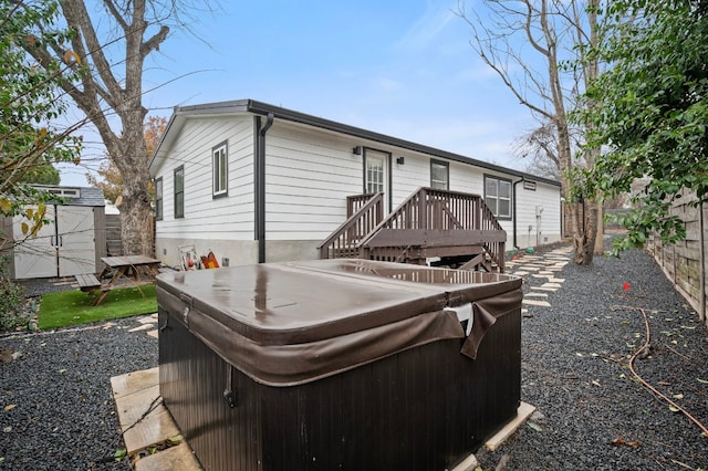 rear view of property featuring a storage shed, a hot tub, and a deck