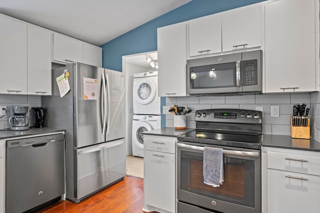 kitchen with stacked washing maching and dryer, appliances with stainless steel finishes, white cabinets, and lofted ceiling