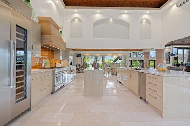 kitchen with a kitchen island with sink, sink, premium appliances, and a towering ceiling