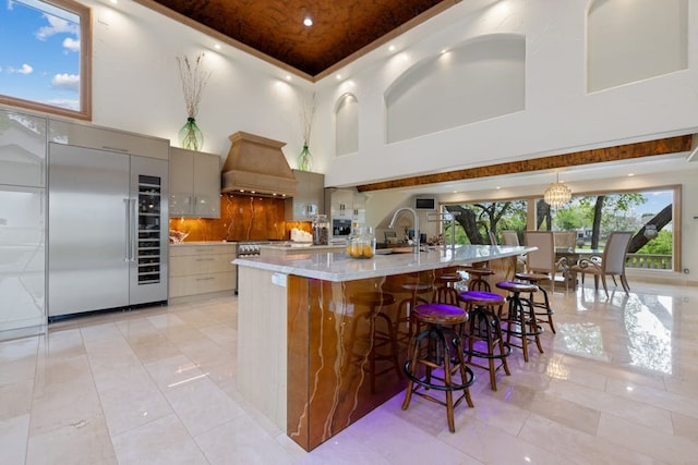 kitchen with pendant lighting, a large island, built in refrigerator, light stone counters, and custom exhaust hood