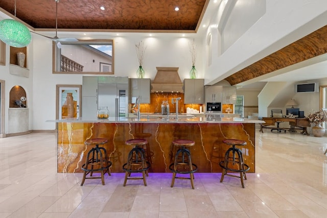 kitchen featuring decorative backsplash, premium range hood, a high ceiling, and built in refrigerator