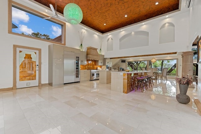 kitchen featuring a towering ceiling, a kitchen breakfast bar, high quality appliances, custom exhaust hood, and a raised ceiling