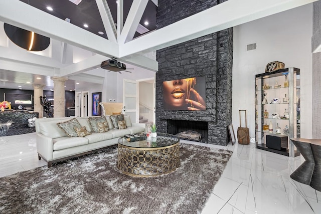 living room with ornate columns, a stone fireplace, a high ceiling, and ceiling fan