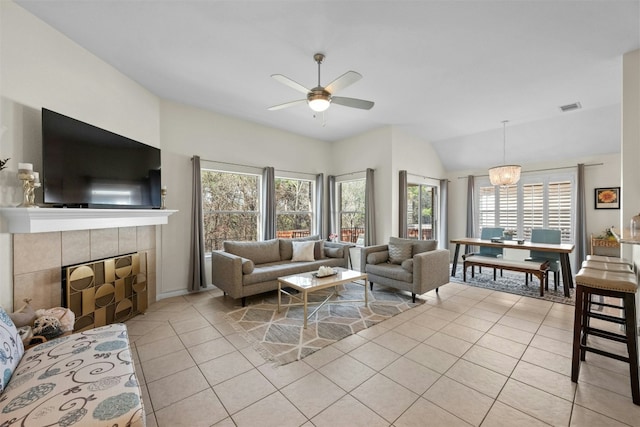 living room with light tile patterned floors, ceiling fan with notable chandelier, vaulted ceiling, and a tile fireplace