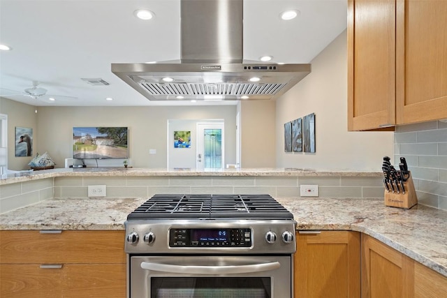 kitchen featuring range hood, tasteful backsplash, ceiling fan, light stone counters, and stainless steel gas range oven