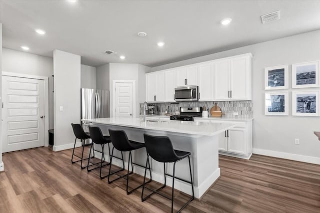 kitchen with white cabinetry, decorative backsplash, appliances with stainless steel finishes, and a center island with sink