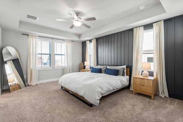 carpeted bedroom with ceiling fan and a tray ceiling