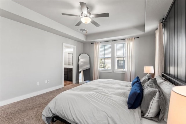 bedroom with a tray ceiling, ensuite bath, light colored carpet, and ceiling fan