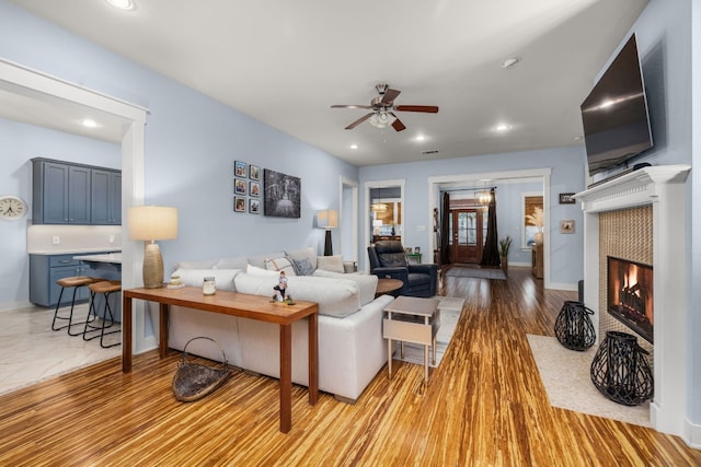 living room with ceiling fan, a tile fireplace, and light wood-type flooring