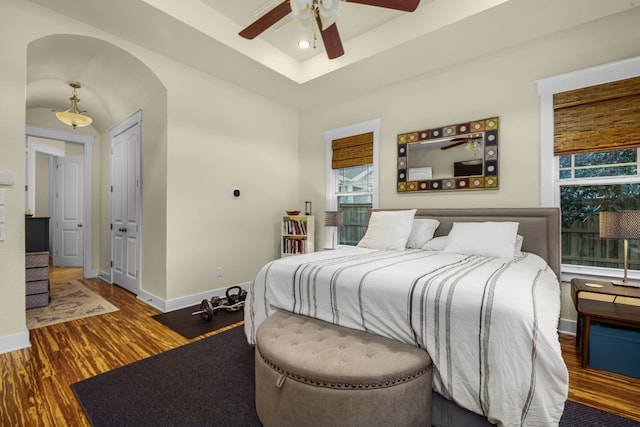 bedroom with a raised ceiling, ceiling fan, and dark hardwood / wood-style flooring