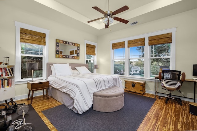 bedroom with ceiling fan, wood-type flooring, and a tray ceiling