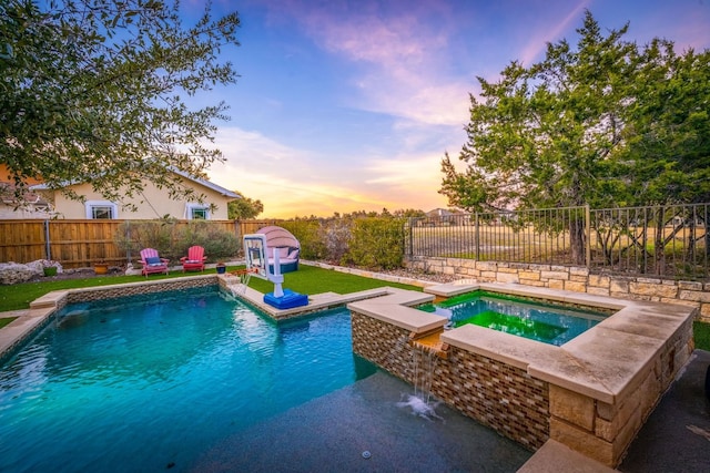 pool at dusk featuring an in ground hot tub and pool water feature