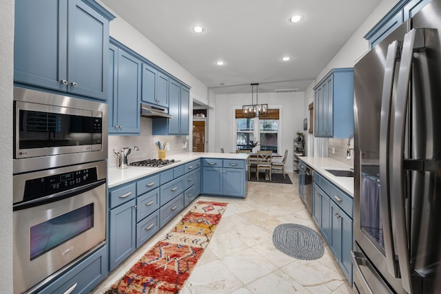 kitchen featuring pendant lighting, appliances with stainless steel finishes, blue cabinets, decorative backsplash, and kitchen peninsula