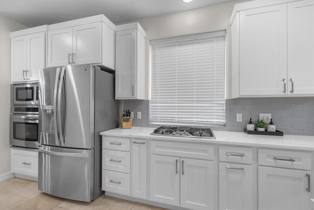 kitchen featuring tasteful backsplash, white cabinets, light tile patterned floors, stainless steel appliances, and light stone countertops