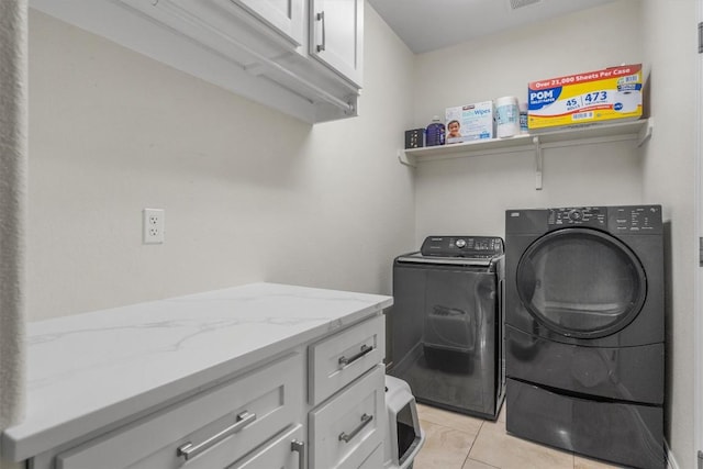 clothes washing area featuring cabinets, light tile patterned floors, and washing machine and clothes dryer