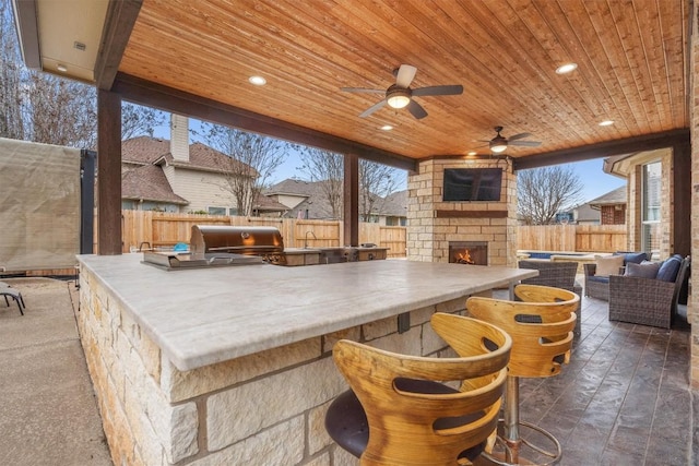 view of patio with area for grilling, an outdoor living space with a fireplace, a fenced backyard, grilling area, and outdoor dry bar