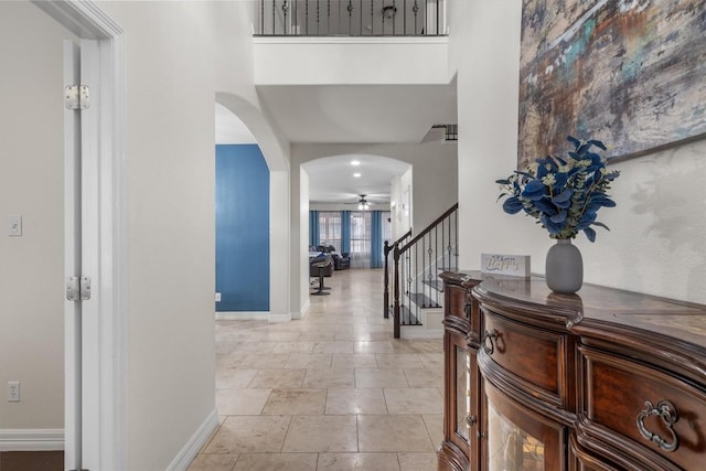 hallway featuring stairs, baseboards, and arched walkways