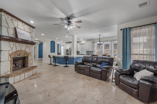 living area with baseboards, visible vents, a fireplace, arched walkways, and ceiling fan with notable chandelier