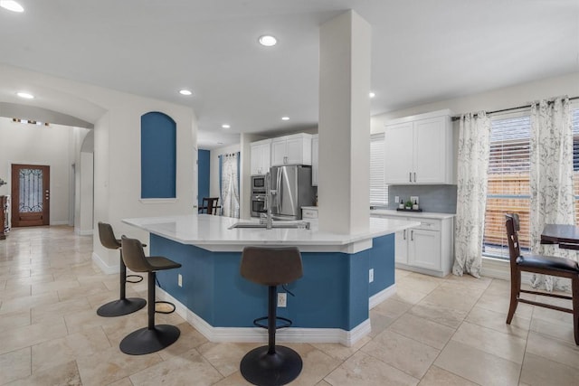 kitchen featuring appliances with stainless steel finishes, tasteful backsplash, white cabinets, a kitchen bar, and a kitchen island with sink