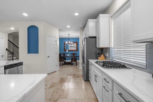 kitchen with hanging light fixtures, stainless steel appliances, white cabinets, and light stone countertops