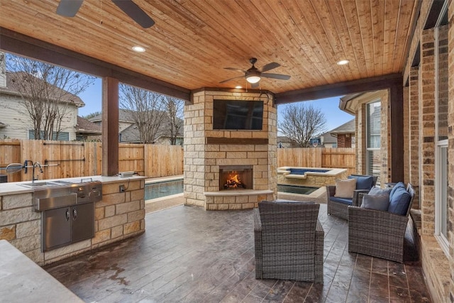 view of patio with ceiling fan, exterior kitchen, an outdoor stone fireplace, and a fenced backyard