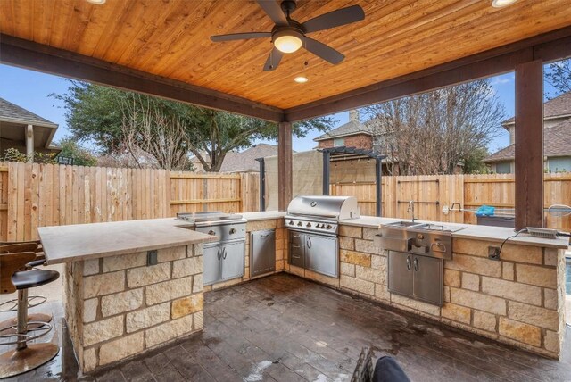 view of patio featuring a grill, an outdoor bar, ceiling fan, and exterior kitchen