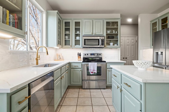 kitchen with sink, light tile patterned floors, appliances with stainless steel finishes, light stone countertops, and backsplash