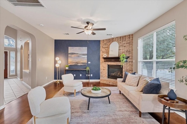 living room featuring a fireplace, wood-type flooring, a healthy amount of sunlight, and ceiling fan