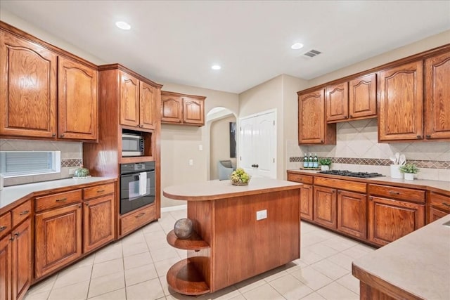 kitchen with appliances with stainless steel finishes, a center island, light tile patterned floors, and backsplash